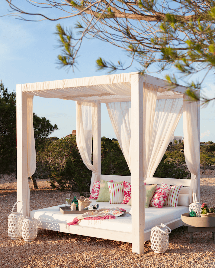Cama balinesa en jardín con cortinas blancas.