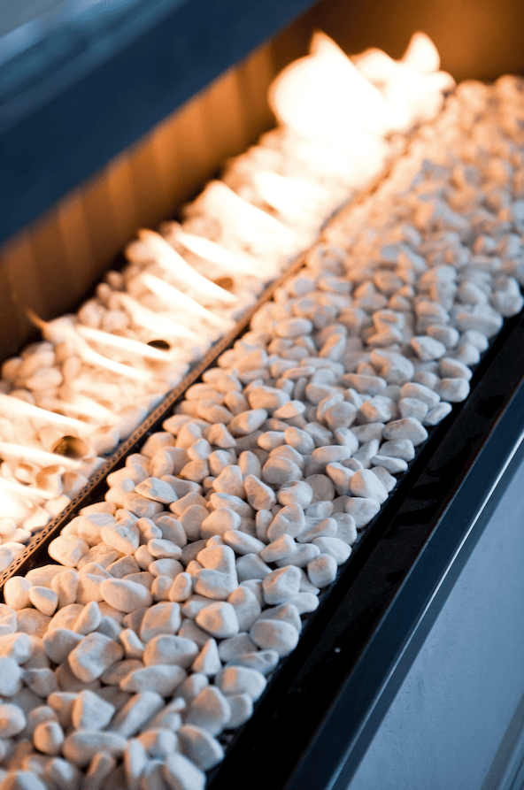 Chimenea decorativa con piedras blancas y fuego lineal.